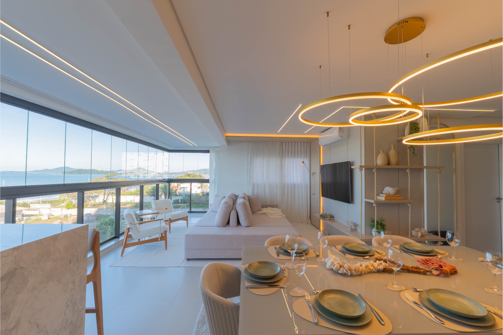 Living com iluminação em anéis suspensos, mesa posta e vista para o mar